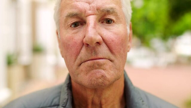 Portrait of a serious senior man outside in a park with copy space. Face of an old grumpy, angry and unsmiling business man standing outdoors in a bright modern city or town with copyspace