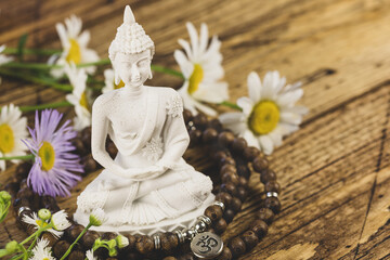 Buddha statue, prayer beads and wild flowers on a wooden background. Asian spa ritual procedure and meditation. Energetic health and relax. Mental healing. Vesak, Buddha Day. Soft focus style