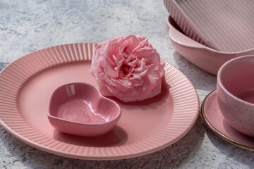 Pink empty plate and pink sauce boat in shape of heart. Pink dishes and utensils for serving and eating meals. On light grey background with marble effect. Modern ceramic crockery, trendy tableware