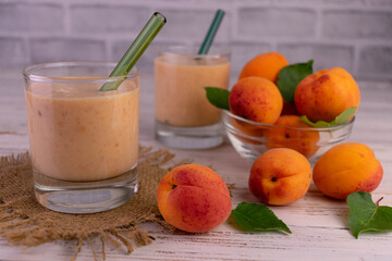 Apricot smoothie in glasses on a white wooden table.

