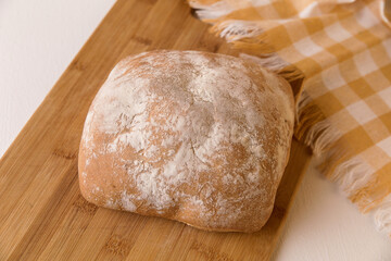 Fresh chabat bread on a wooden board, next to a yellow towel on a light background