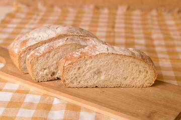 Fresh chabata bread cut into pieces on a wooden board, yellow towel, minimalism