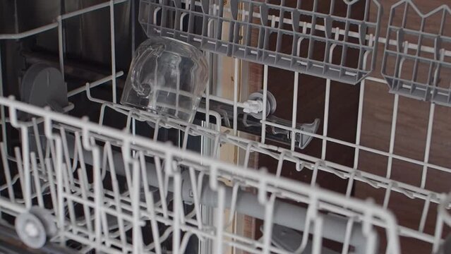 Close-up of female hands opening dishwasher with crystal clear glasses. Top view. Cleaning dirty dishes. Woman fills the upper level of the dishwasher with dirty dishes, glasses. Slow motion
