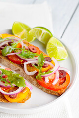Vegetarian toasts and lime on a white plate. Bruschetta with tomatoes, greens and olives. Healthy open sandwiches on white boards. Top view