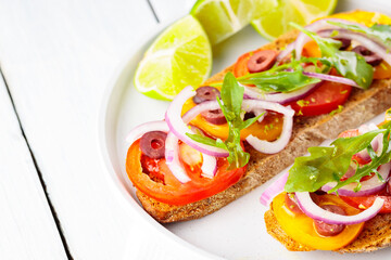 Vegetarian toasts and lime on a white plate. Bruschetta with tomatoes, greens and olives. Healthy open sandwiches on white boards. Top view