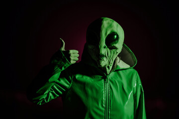 Alien showing thumb up. Like gesture. Creepy mask of humanoid on neon planet in smooth raincoat....