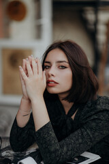 a brunette girl in a short dark dress and black glasses sits on a chair in a cafe in the city