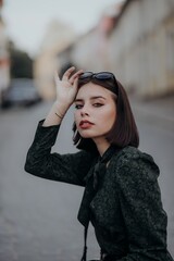 a brunette girl in a short dark dress and black glasses walks down the road in the city