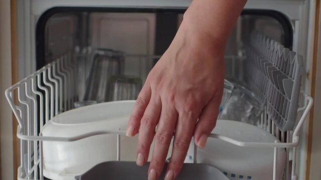 Housewife puts dirty dishes in the dishwasher. Female hands unload the dishwasher in close-up. Modern household appliances at home. Woman puts the top baskets with dirty dishes in the dishwasher. Slow