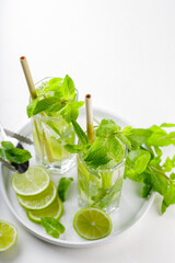 Mojito cocktail and bar tools on a white background. Two glasses of mojito with mint and lime on a white plate. Summer drink with bamboo straw