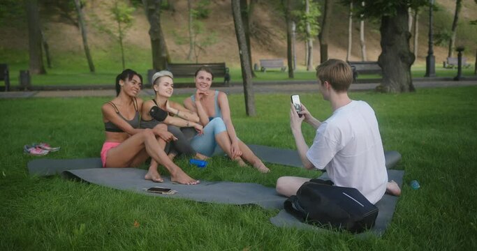 Guy photos athletic women friends sitting on park grass