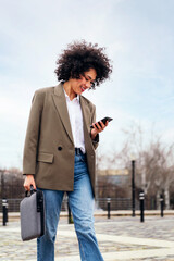 smiling young business woman walks using a smart phone in the city, technology and communication...