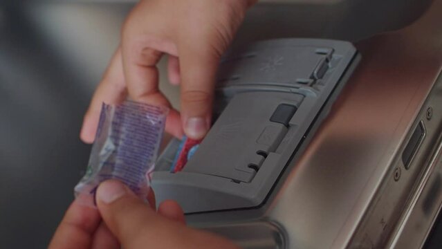 Caucasian young guy, a teenage boy puts a tablet of detergent in the dishwasher. Close up of guy hands. Helps mom with household chores. Modern household appliances at home. Slow motion