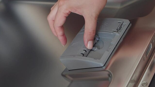 Caucasian woman puts a tablet of detergent in the dishwasher. Close up of woman hands. Modern household appliances at home. Slow motion. Female hands unload the dishwasher in close-up