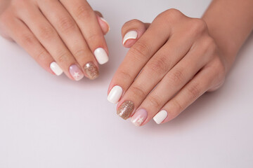 Obraz na płótnie Canvas Beautiful female hands with romantic manicure nails, white and pink gel polish with golden glitter 