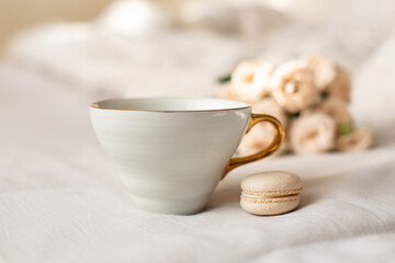 Sweet dessert, vanilla macaroons, mug and white roses on bed background. Romantic morning breakfast at bed.