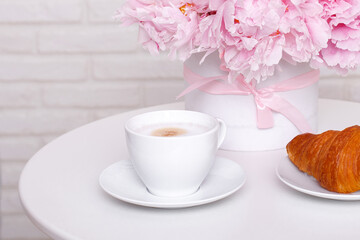Cup of coffee and croissant with peonies flowers on white table