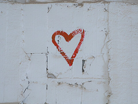 red paint drawing of a heart shape on the white brick wall background