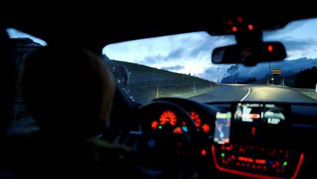 A man drives a car on a twisty country road at sunrise with an illuminated dashboard and navigation.