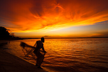 Naklejka na ściany i meble A Fisherman Catching in fish On Sea Against orange Sky During Sunset