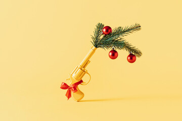 Yellow gun with green Christmas tree branch, decorations and red balls. Party New Year 2023 minimal...