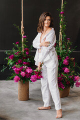 A gentle and peaceful brunette woman in white clothes in a room with peonies 