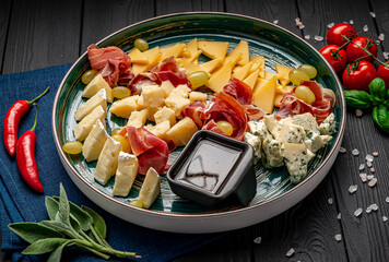 Cheese platter with different cheese, jamon, prosciutto and grapes.