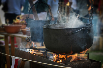 Large iron kettle or caldron with steaming stew over fire, food for all on a pristine outdoor...