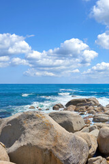 Copyspace at sea with a cloudy blue sky background and rocky coast in Camps Bay, Cape Town, South Africa. Boulders at a beach shore across a majestic ocean. Scenic landscape for a summer holiday