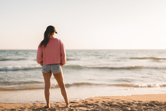woman in sweatshirt and cap watches the sunset on the beach