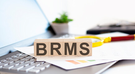 BRMS - Business Rules Management System written on a wooden cube on a laptop with paper