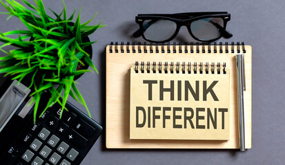 Word THINK DIFFERENT on notebook with pencil on grey background