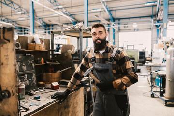 A workshop worker holding a hammer and smiling at the camera at shop.
