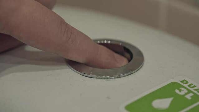 Man's finger presses the toilet flush button. Hygiene in the toilet after yourself. Ceramic plumbing. Master checks the serviceability of home equipment after repair or installation.