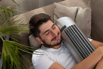 image fun et amusante d'un jeune homme qui embrasse son ventilateur pendant la canicule. Il est allongé dans son canapé et il fait chaud.