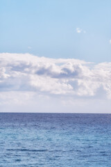A cloudy blue sky and peaceful, calm ocean separated by a beautiful horizon with copy space. Deep blue water underneath a cloudscape skyline. The many tides, currents and waves in the wide open sea