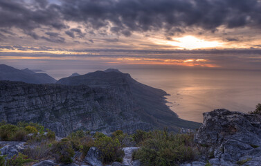 Fototapeta na wymiar Above view of a mountain coastline at sunset in South Africa. Scenic landscape of dark clouds over a calm and peaceful ocean near Cape Town with the sun behind grey clouds in the sky and copy space