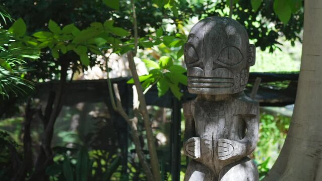 This panning video shows a wood carved tiki statue in a rainforest jungle. 