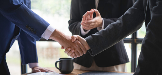 Business team shaking hands and clapping after a business deal Image of business partners handshaking over business objects in the office