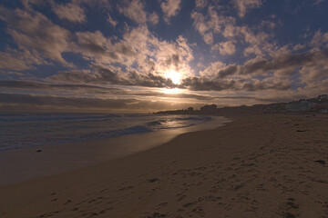 puesta de sol contra el sol en la playa con nubes en el horizonte