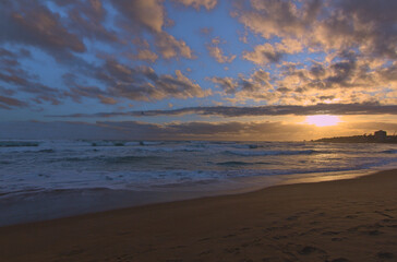 Fototapeta na wymiar puesta de sol en la orilla de la playa con ciudad de fondo, lente gran angular