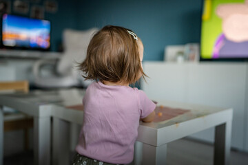 Fototapeta na wymiar Back view of one unknown caucasian child toddler girl standing at home watching tv while eating copy space childhood growing up development leisure concept