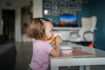 one girl small caucasian toddler female child daughter eating alone at the table at home while watching tv making mess on her face dirty sauce childhood growing up development concept copy space