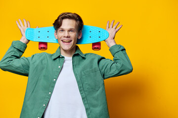 happy guy posing on yellow background holding blue skateboard behind his head