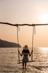 Traveler woman relax on swing in the sea between sunset at the beach