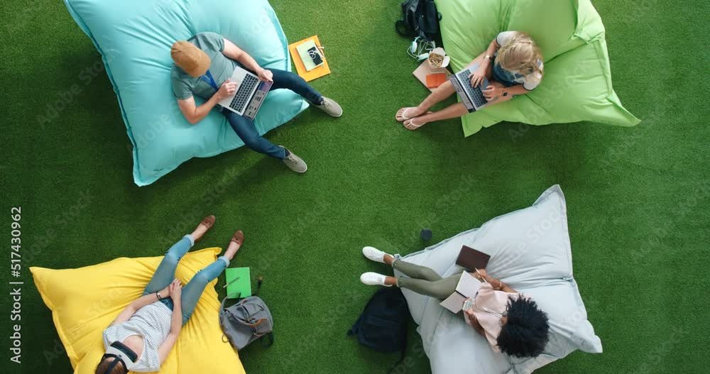 Aufkleber Students using modern technology and sitting on bean bag in a library from above. Bright informal office space to improve creativity and mindfulness. Spot for staff to relax and browse the internet