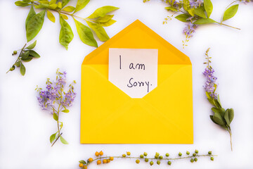 i am sorry message card handwriting in yellow envelope with flowers arrangement flat lay style on...