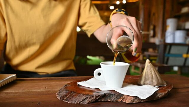 Woman pouring brewed coffee from jar into shot glass before drinking. Brewed coffee is made by pouring hot water onto ground coffee beans.
