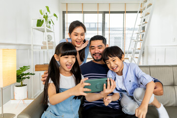 Asian family using tablet, laptop, phone for playing game or movies, relaxing at home for...