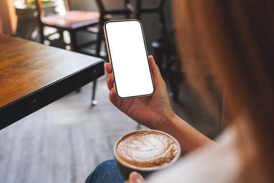 Mockup image of a woman holding mobile phone with blank desktop screen while drinking coffee